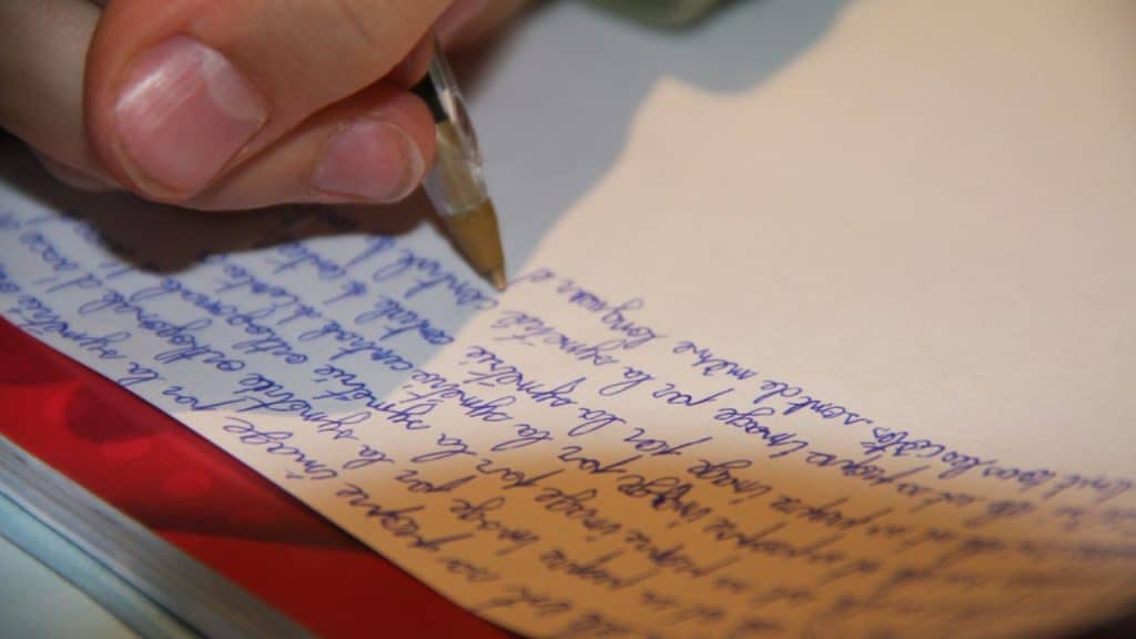 Close-up shot of a hand writing blue cursive script on a piece of paper with a ballpoint pen.
