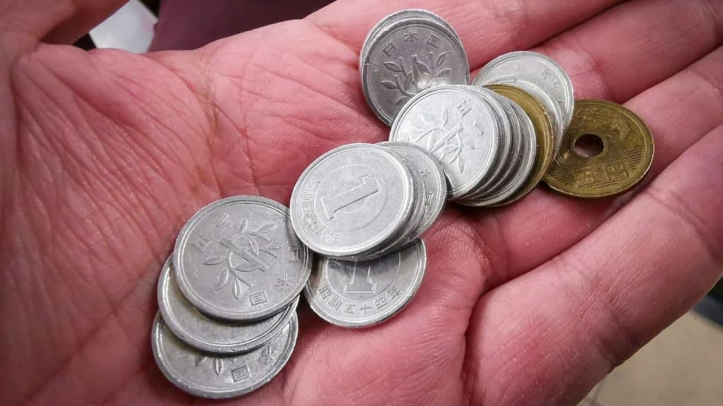 Close-up of a person's palm holding a pile of Japanese yen coins, mostly silver-colored.