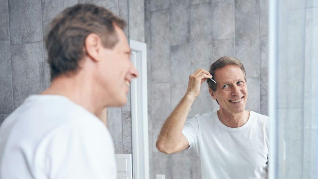 A smiling middle-aged man fixing his hair while looking in a mirror.