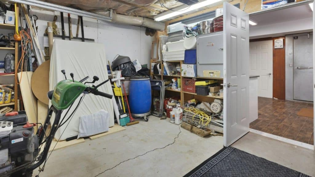 A cluttered storage room or basement filled with tools, boxes, a blue barrel, and a green yard machine.