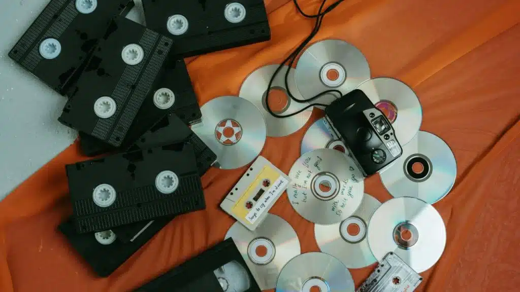Overhead view of a collection of VHS tapes, CDs, audio cassette tapes, and a small black camera on an orange cloth.