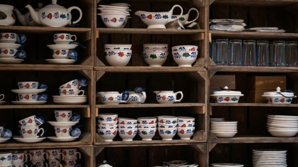 Rustic wooden shelves displaying white ceramic dishes decorated with red, green, and blue floral patterns.