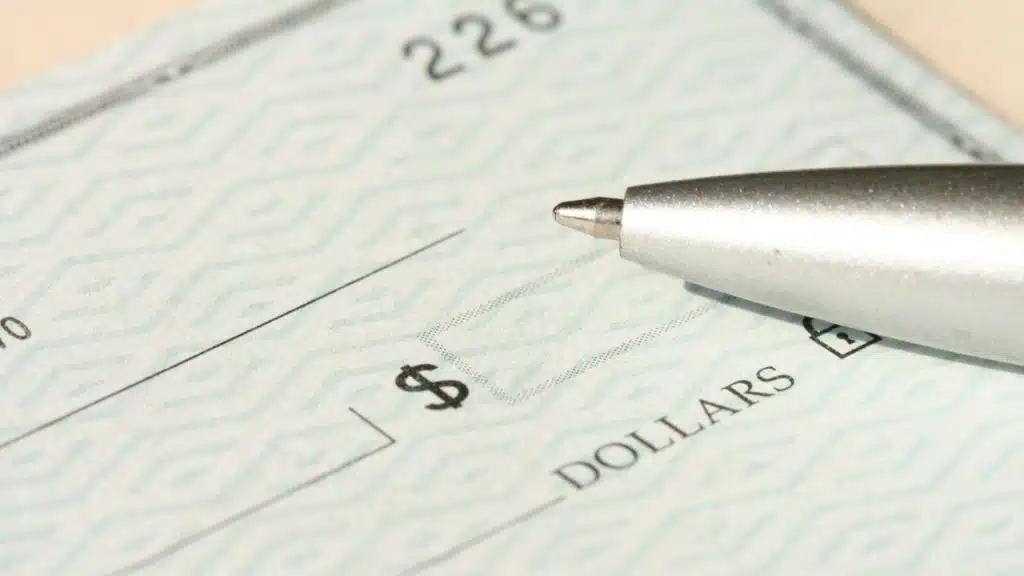 Close-up of a silver pen nib hovering over the dollar sign on a blank bank check.
