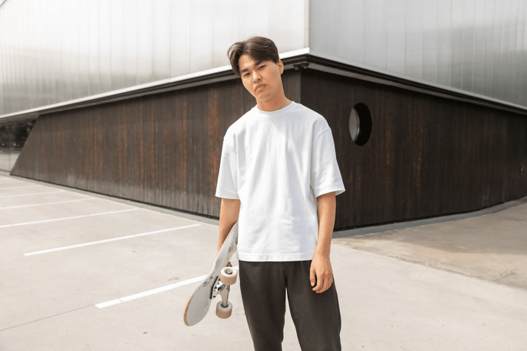 Confident young Asian man standing near modern building with skateboard in hand