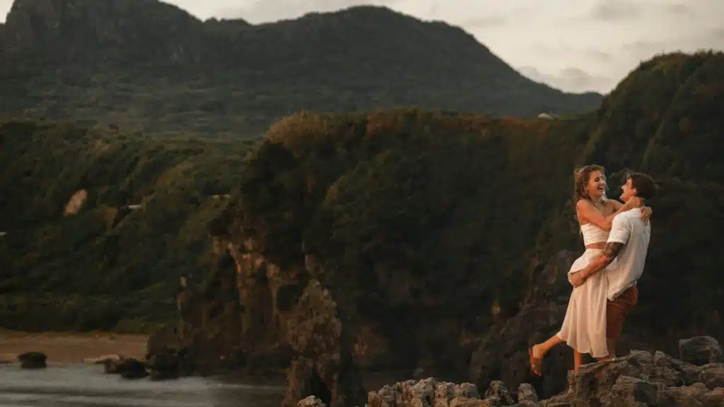A couple standing at the edge of a cliff with beautiful scenery in the background.