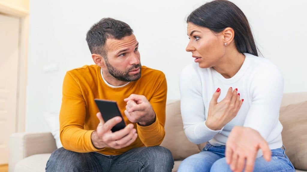 Husband asking for an explanation to his cheater wife sitting on a couch.