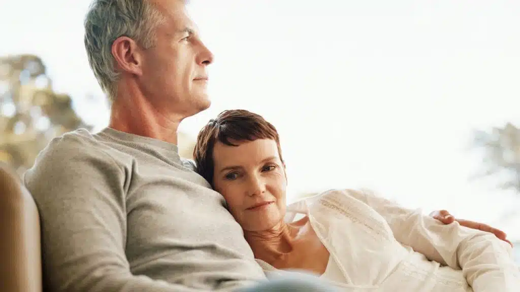 A mature couple with the woman resting her head on the man’s chest.