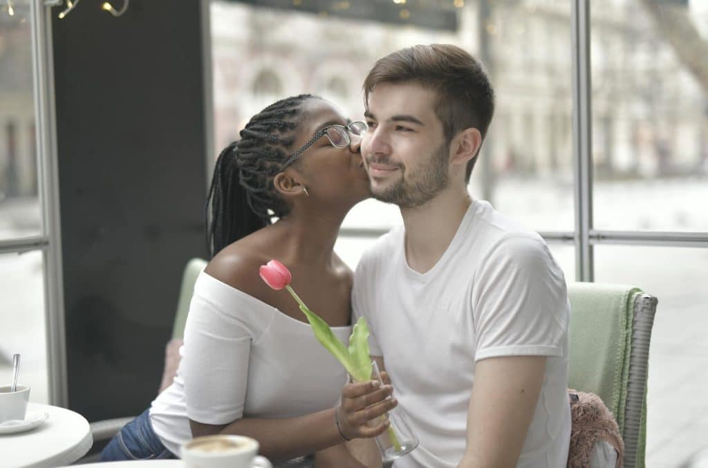 The woman holding a flower is kissing the man on the cheek.