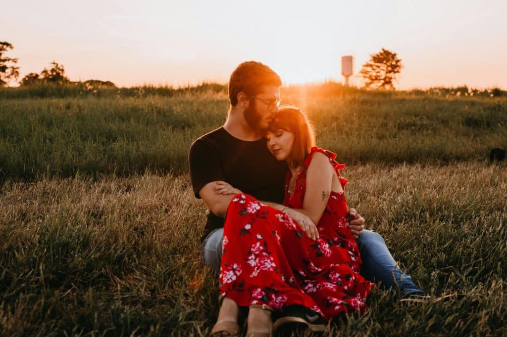 The couple is sitting on the grass while hugging each other.
