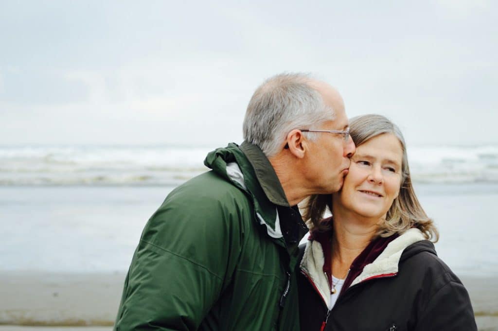 The man is kissing the woman beside the beach.