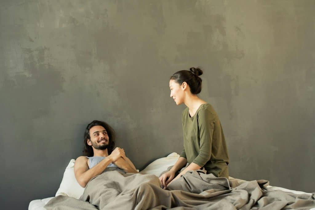 The man and woman are smiling while talking to each other in the bed.