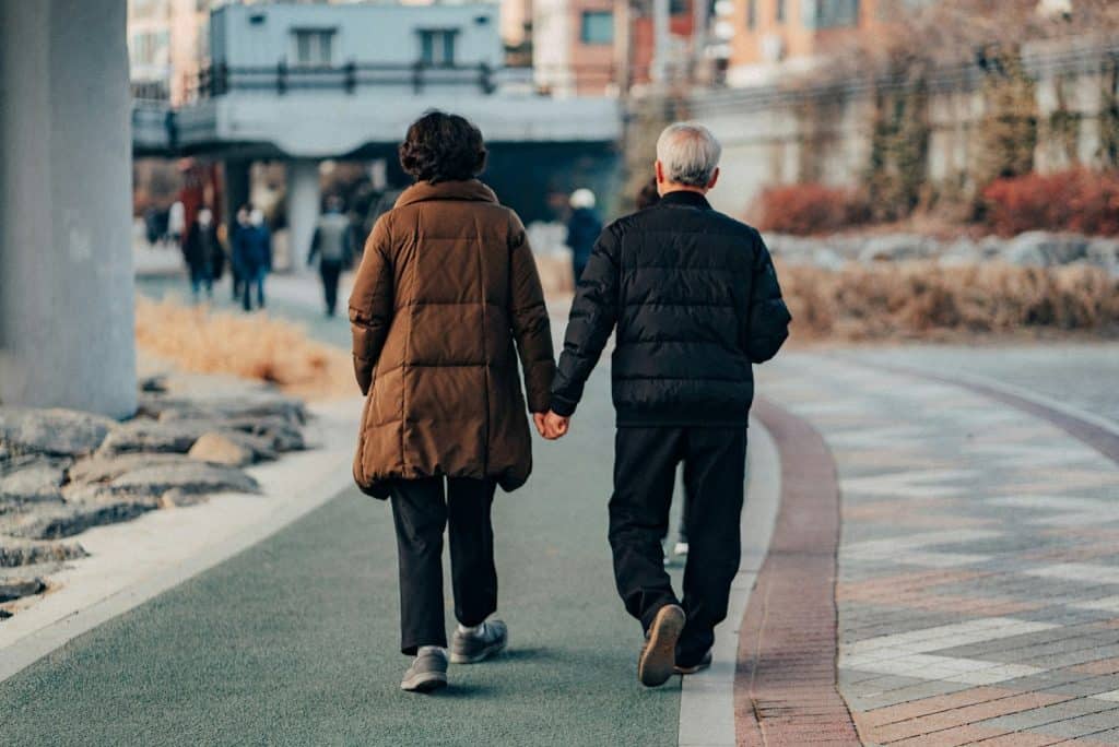 The couple is walking on the sidewalk while holding hands.