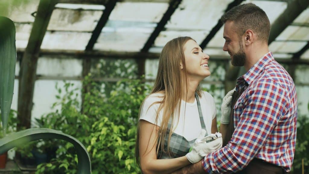 The couple is embracing in the greenhouse.