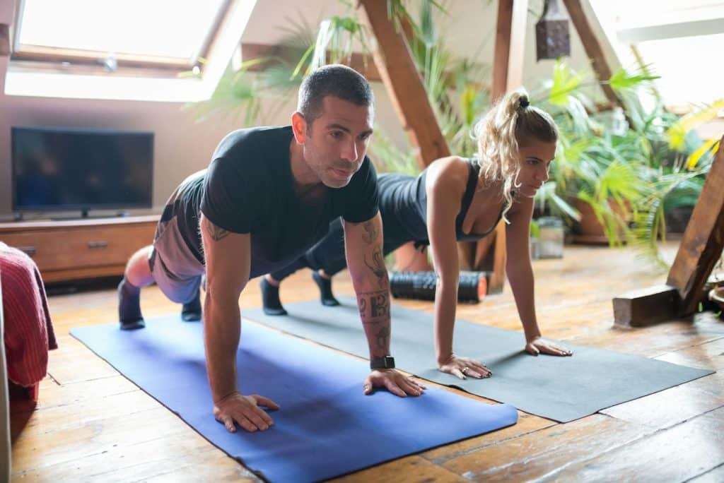 The couple is doing push ups together at home.