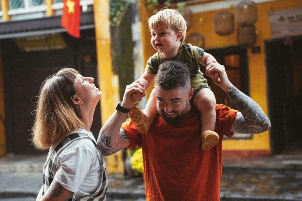 A couple on the street with the father carrying their son on his shoulders.