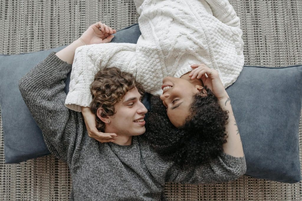 A couple lying on the floor looking at each other and smiling.