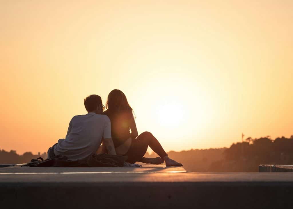 A couple sitting beside each other and looking at the sun during golden hour.