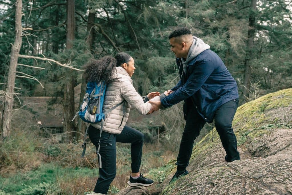 A couple taking a hike in the mountains and helping each other.
