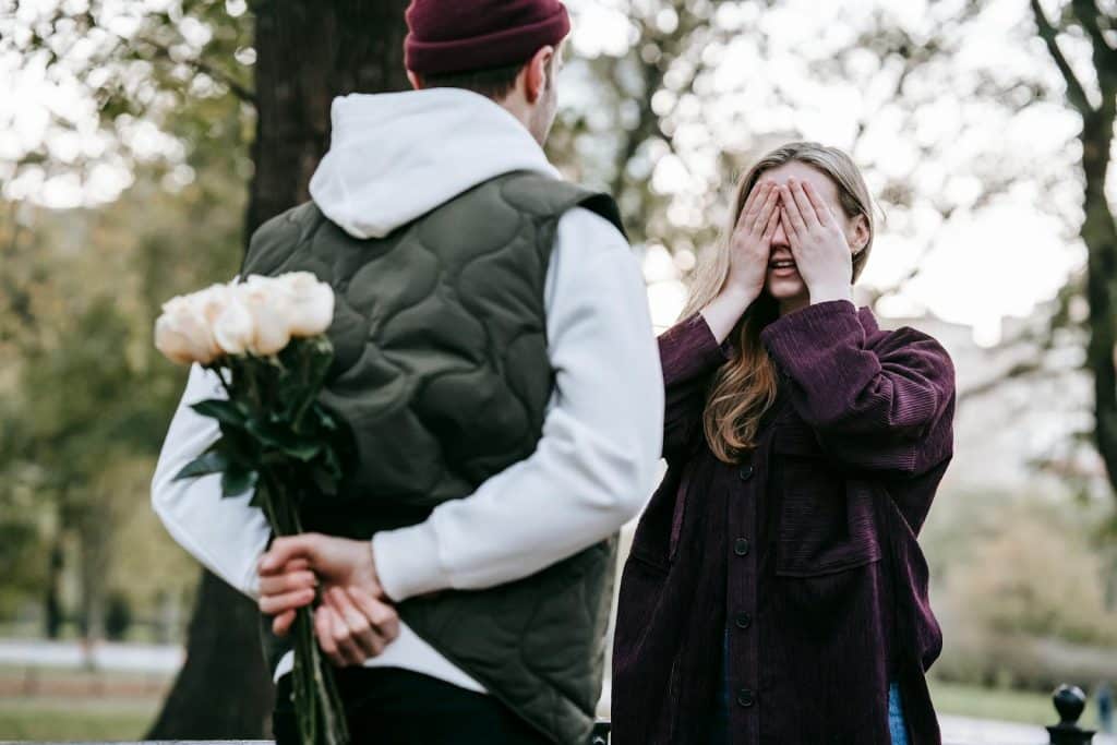 The man is surprising the woman with flowers.