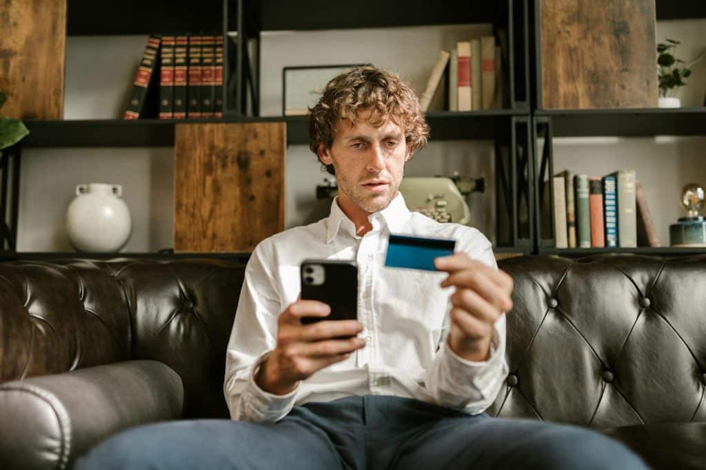 The man is holding a phone and a credit card.