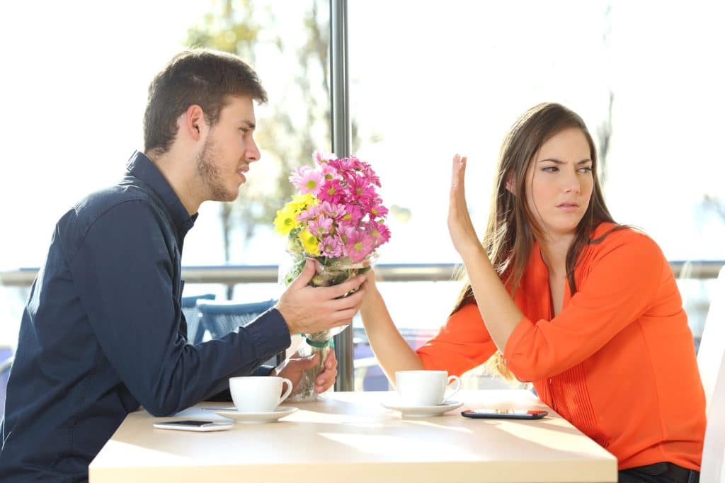 The woman is ignoring the man who is giving her flowers.