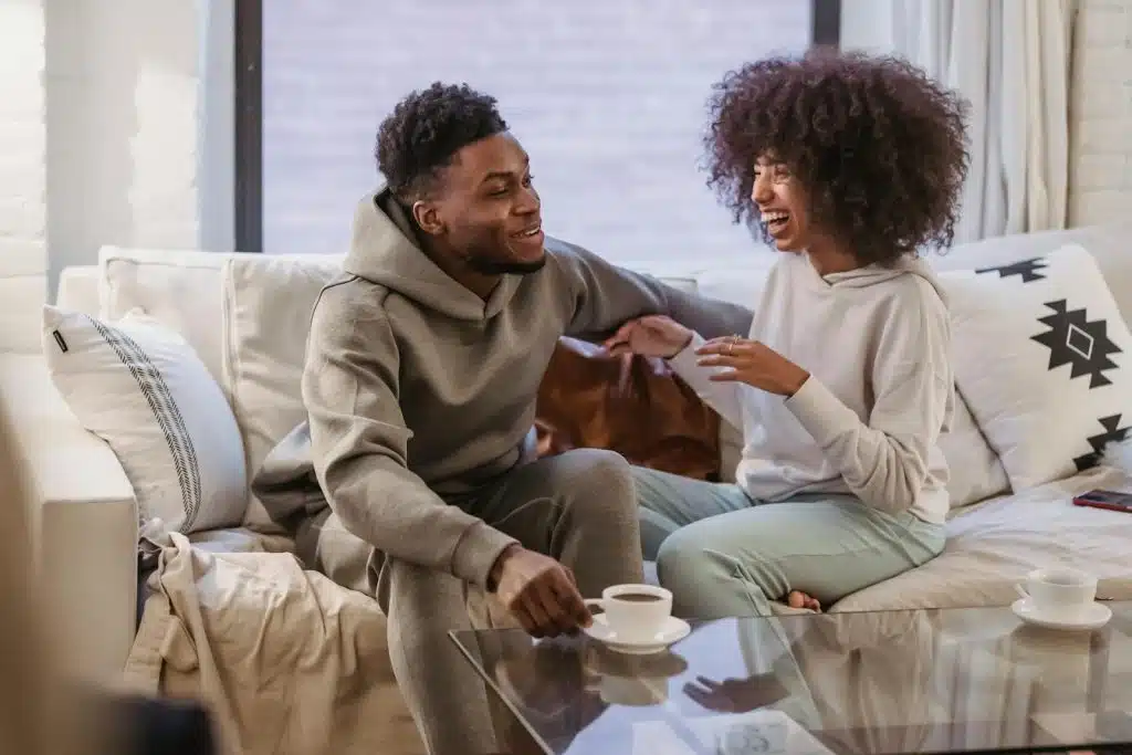 The couple is sitting on the couch, talking to each other.