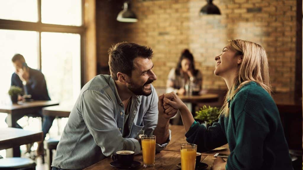 A couple laughing while holding hands at a cafe.