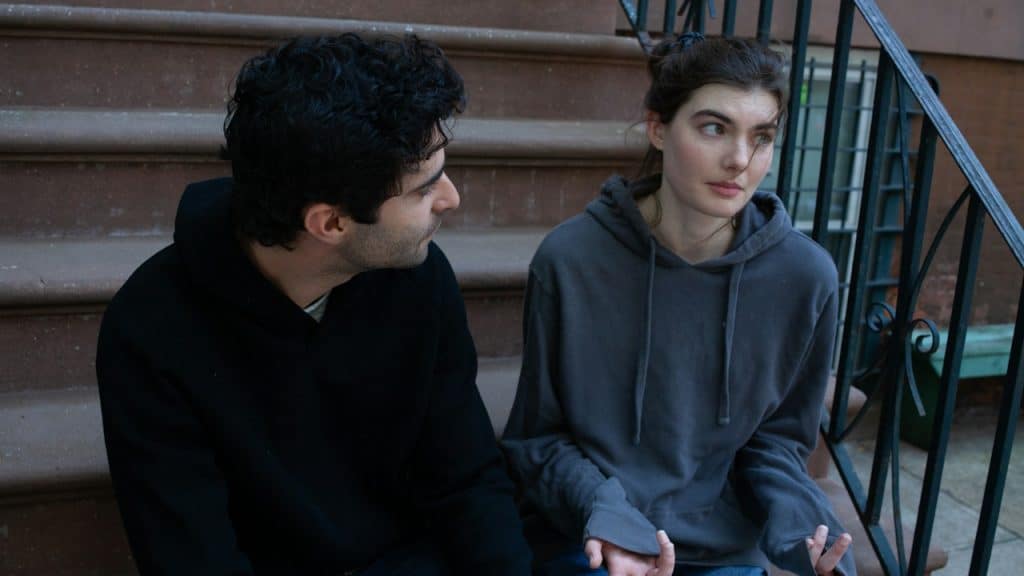 A couple sitting on stairs with the woman rolling her eyes to the side and gesturing with her hands.