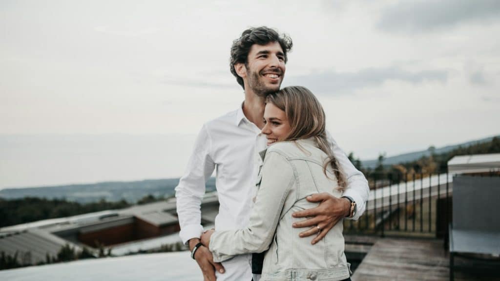 A couple hugging on top of a building with the cityscape visible in the background.