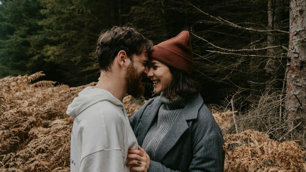 A couple smiling and touching foreheads in the woods.