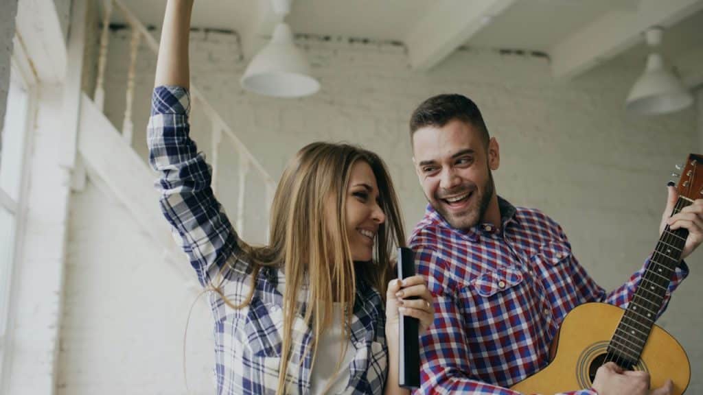A couple having fun with the man playing a guitar and the woman singing.