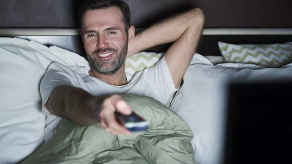 Man turning the TV off before sleeping in a dimly lit bedroom