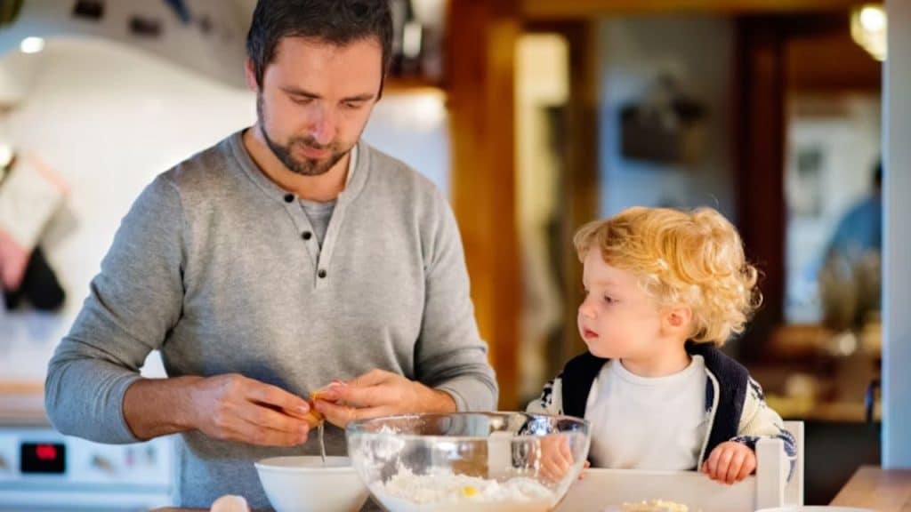 Husband taking care of a kid while cooking breakfast