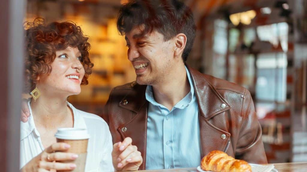 A couple smiling and talking while having coffee and pastries at a café.