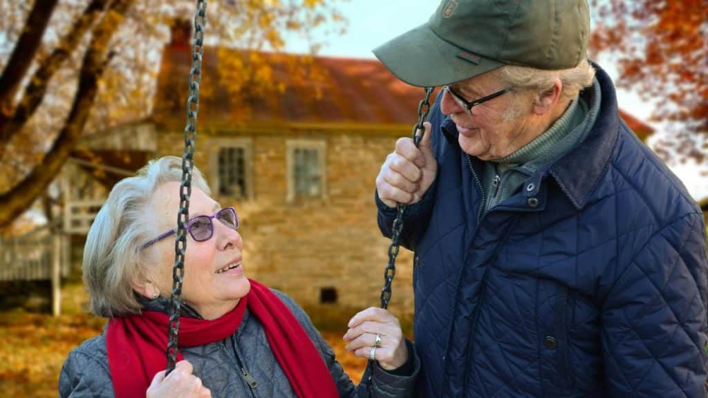 A senior couple smiling at each other while holding a swing outdoors.