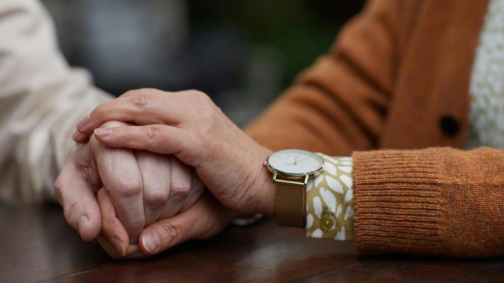 An elderly couple holding hands across a table.