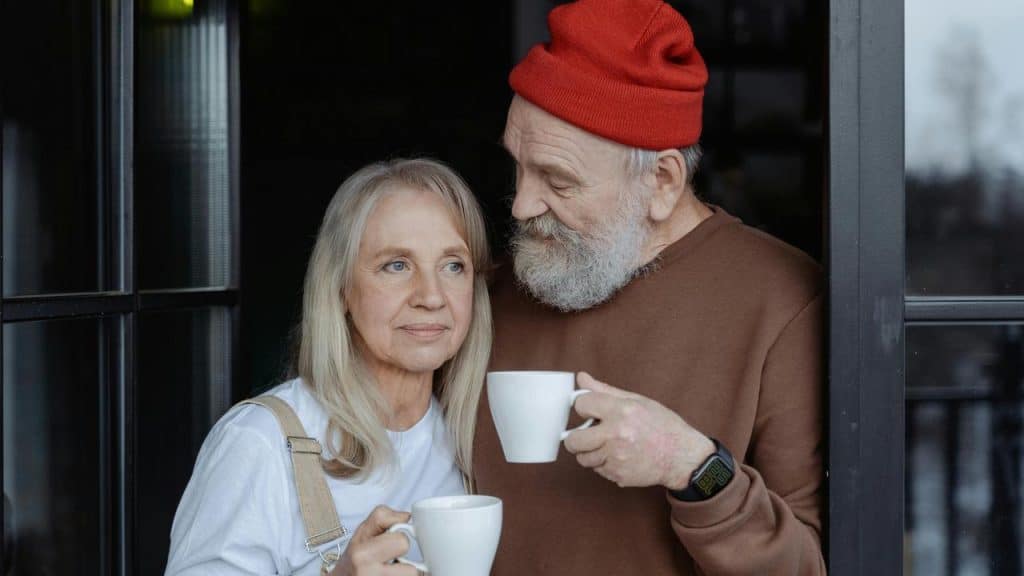 An elderly couple standing together and holding coffee cups.
