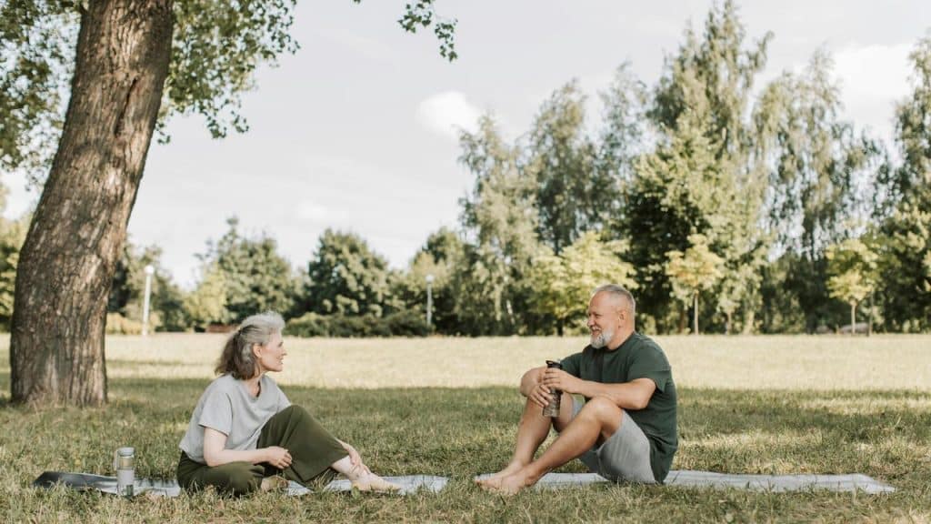 An older couple sitting on yoga mats and talking in a park.