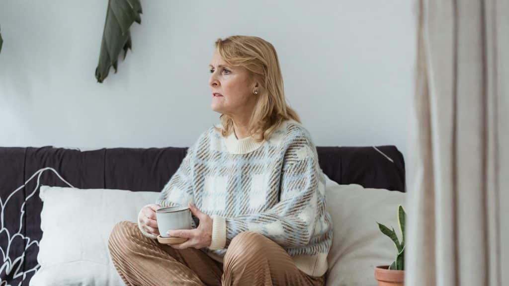 An older woman sitting on a couch and holding a mug.