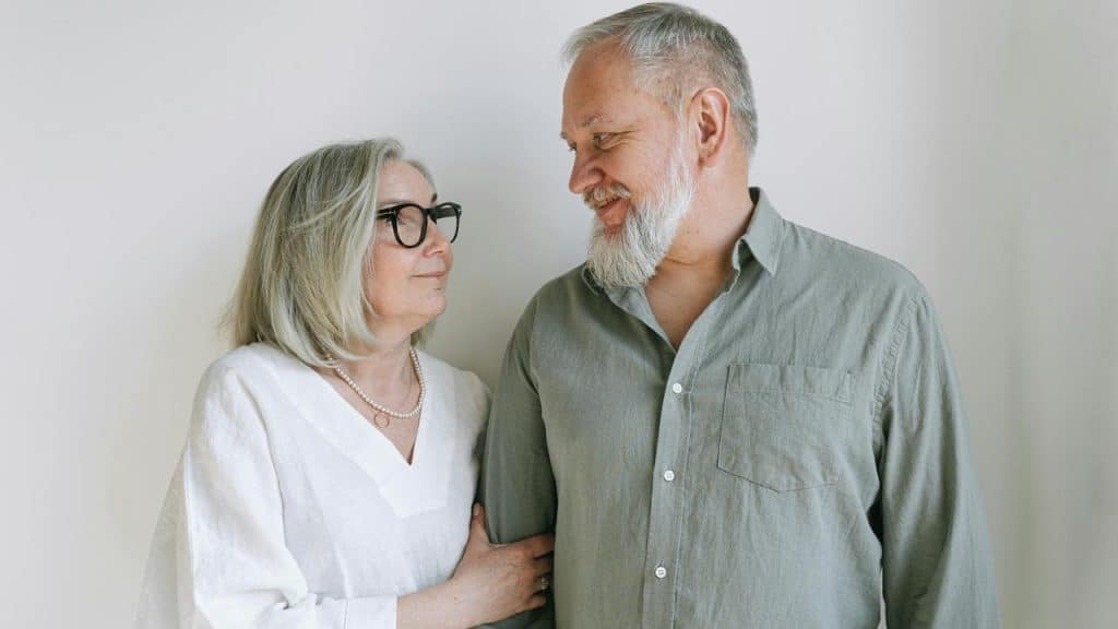 An elderly couple standing close together and smiling at each other.