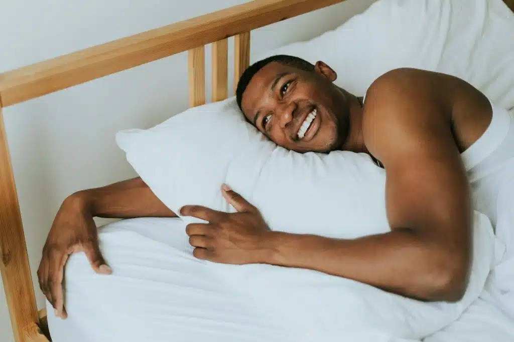 The man is hugging his pillow while smiling.