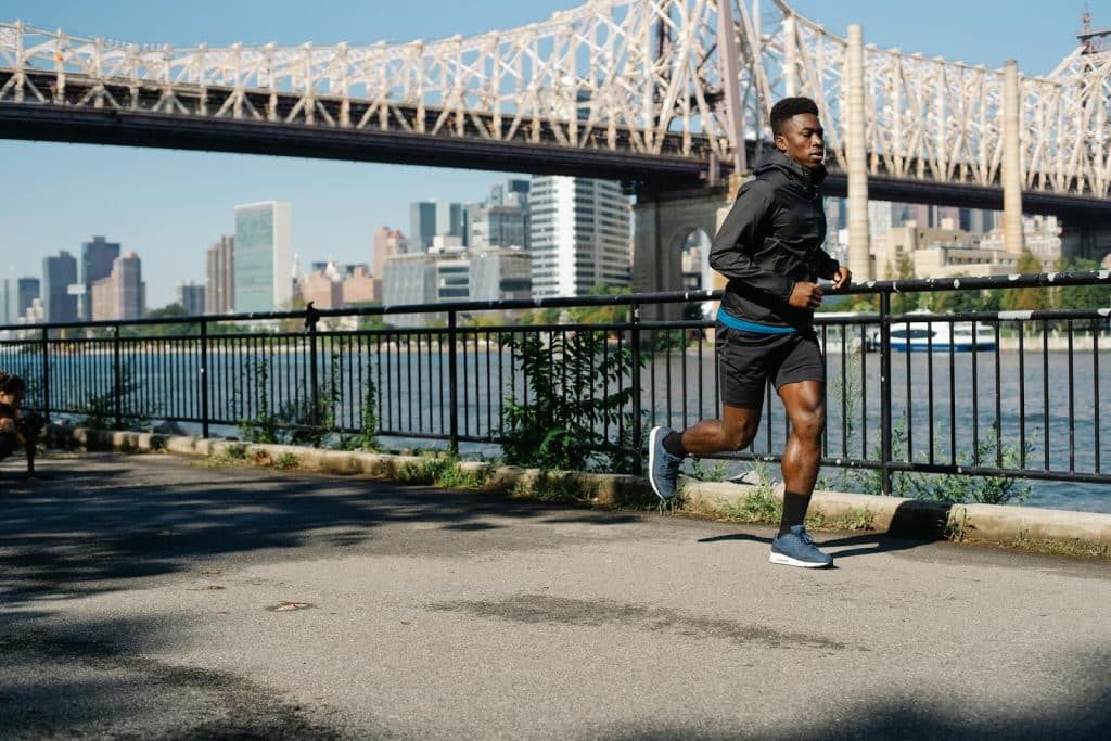 The man wearing black jacket is jogging on the street.