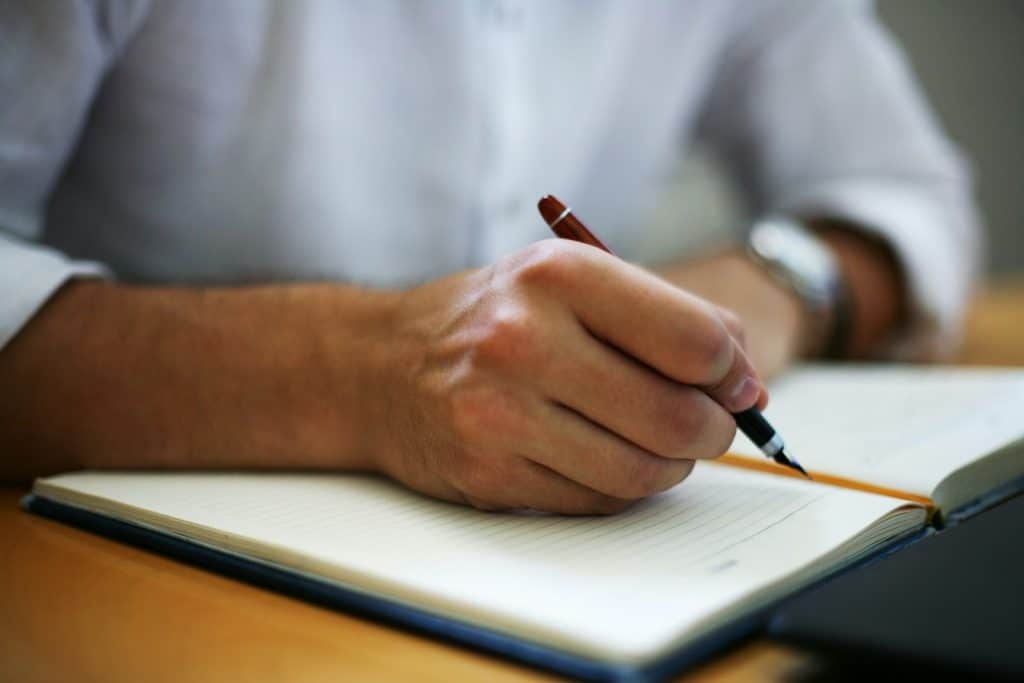 The man is holding a pen, writing this in his notebook.