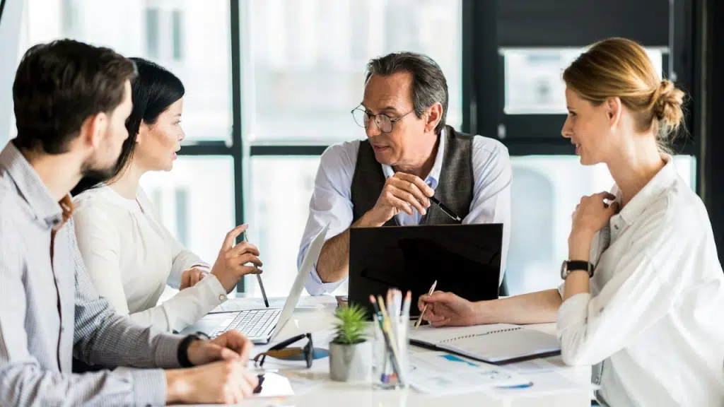 Four people, two men and two women, are engaged in a business discussion around a table.