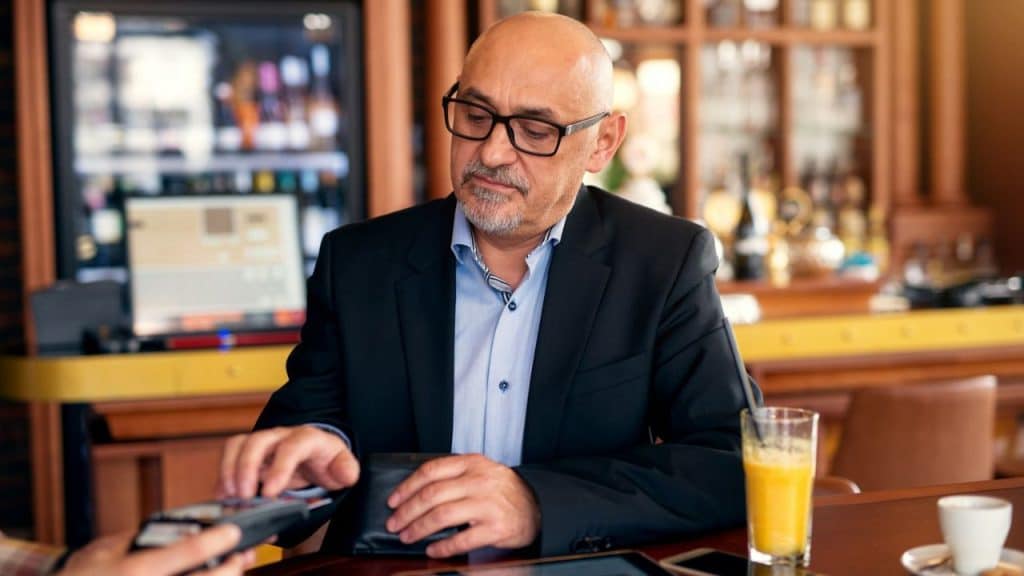 A man in a suit and glasses is using a credit card machine at a bar counter.
