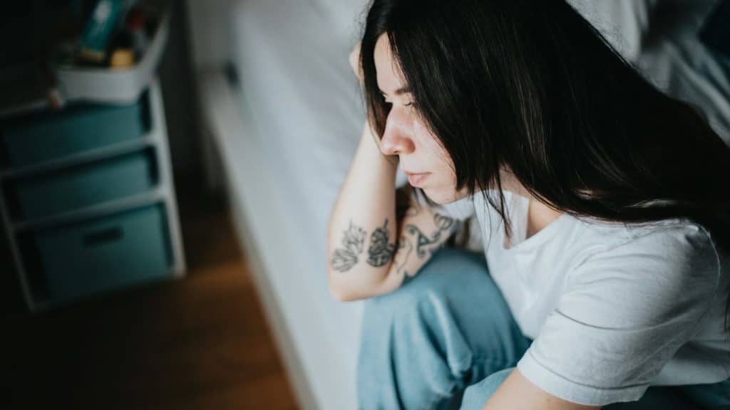 A woman with long dark hair sits on the floor, resting her head on her hand.