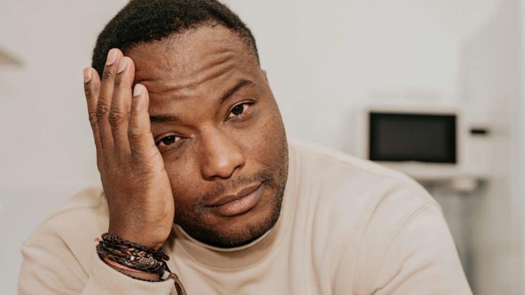 A Black man is resting his head on his hand, looking at the camera with a solemn expression.
