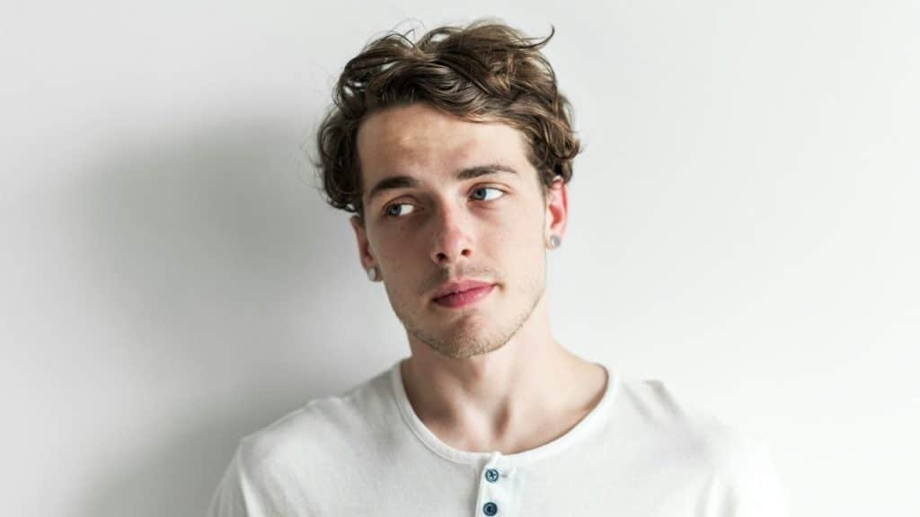 Young man with wavy hair and ear gauges looking slightly up and to the side.