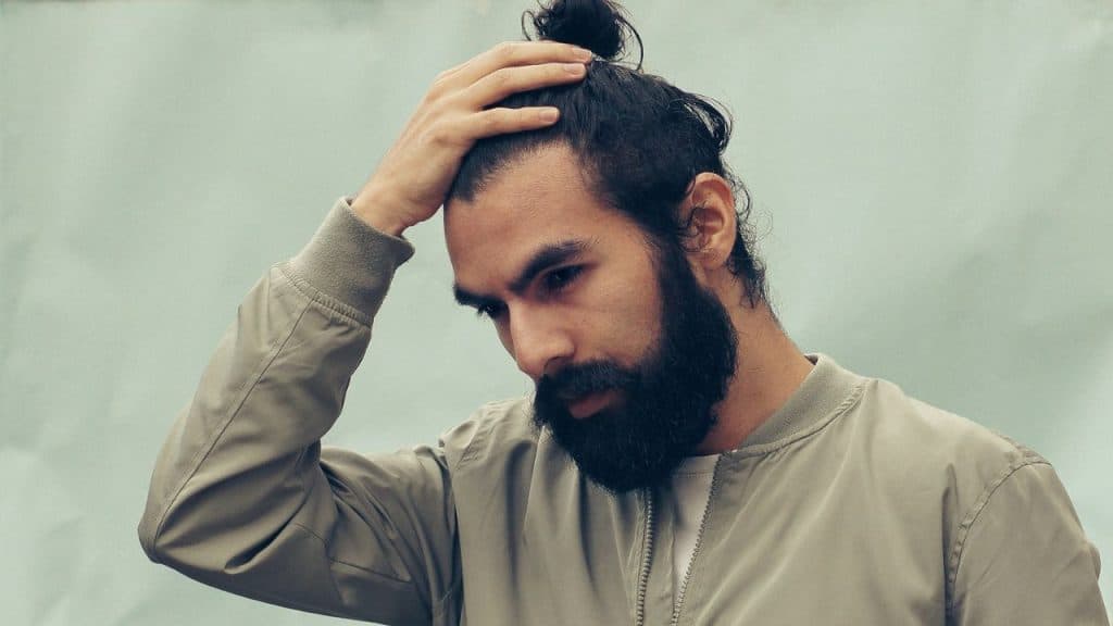 Man with a full beard and a top knot, running his hand through his hair.