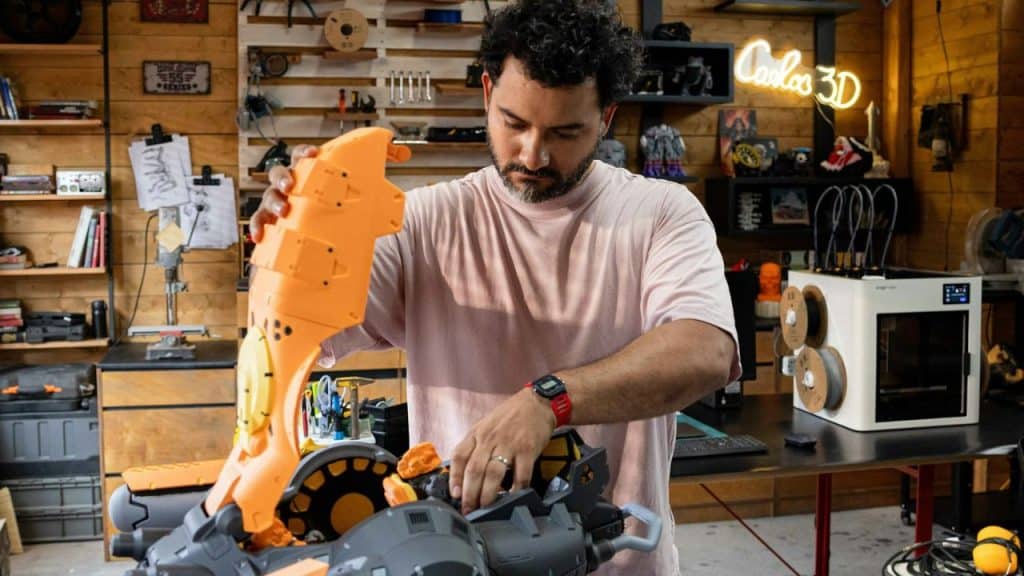 Man working on assembling a large orange and gray plastic model in a workshop.